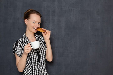 Portrait of happy girl holding coffee cup and croissant in hands