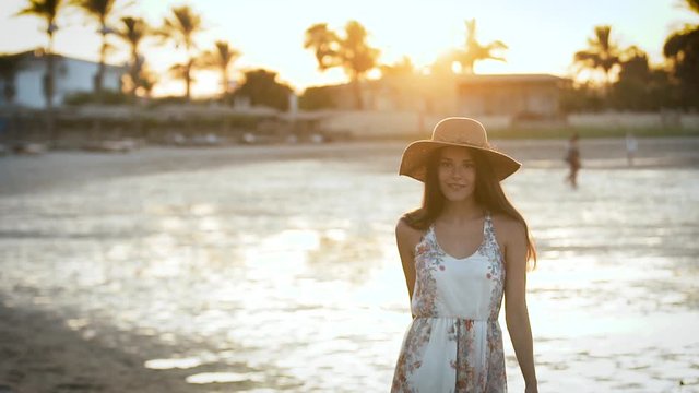 Girl at sunset wears a hat and looks into the sea