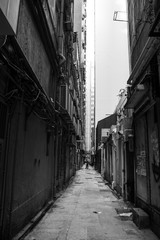 Fototapeta na wymiar Hong Kong narrow street. Scary black and white photography of a very narrow and dirty street in the city center of HK. Vertical composition shot.