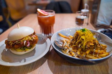 Little Bao delicious chicken burger close up, homemade fries with truffle sauce and yellow lettuce, fresh ice tea. White bun with chinese sauce on a white plate. Best asian burger ever. Not vegan.