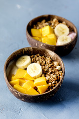 Granola With Yogurt Banana and Mango Tasty Healthy or Diet Breakfast Vertical Coconut Bowls Blue Background