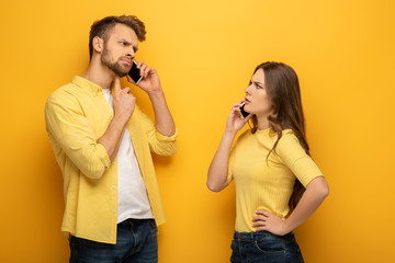 Skeptical couple talking on smartphones on yellow background