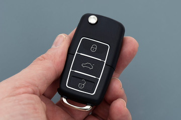 Man hand holding a car key remote on the gray background.
