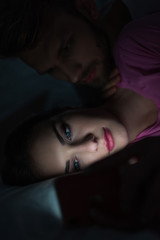 Naklejka premium Selective focus of man embracing smartphone dependent woman on bed at night
