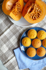 Pumpkin muffins and fresh pieces of pumpkin on blue plate on table with tablecloth, homemade bakery