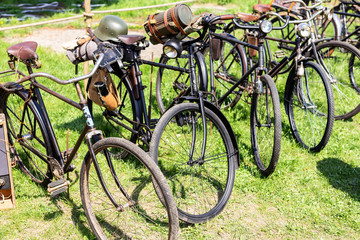 Fototapeta na wymiar Many old rusty vintage retro german military bicyles stand in row on open air parking at city park. World war 2 bike transport exhibition or flea market on sunny day outdoors