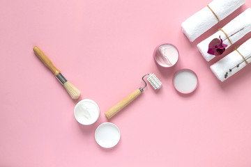 Fototapeta na wymiar Home beauty essentials concept. Self-care in quarantine and self-isolation. Spa and cleanliness concept. Pink background, beauty brush, facial massager, cream, mask, white towels. Copy space. 