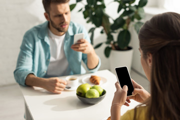 Selective focus of woman using smartphone near boyfriend chatting during breakfast