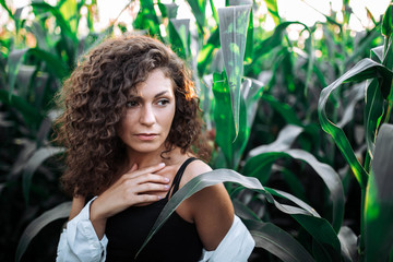 curly swarthy girl in summer corn leaves, art portrait of a woman on nature.