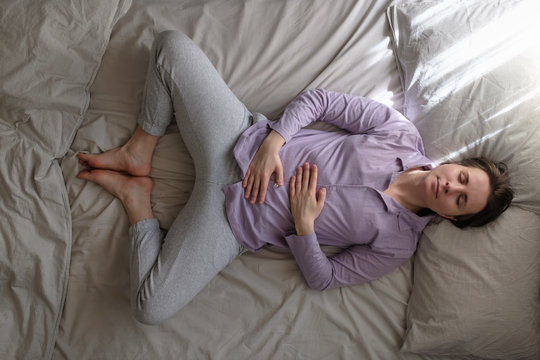 Yoga woman doing supta baddha konasana on bed in the morning breathing.