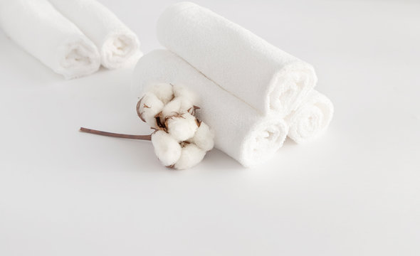 Home beauty essentials concept.  Self-care in quarantine and self-isolation.  Spa and cleanliness concept. On a white background folded in a roller white towels, a branch with cotton flowers.