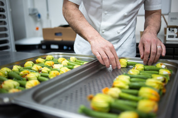 A chef places baby courgettes / zucchinis with flowers stuffed on steal trays, ready to be baked in the oven