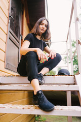 Beautiful stylish brunette girl in a black T-shirt and pants on the stairs. Vertical photo