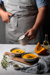man pours cream into pumpkin soup in a ceramic bowl 