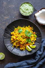Indian cuisine. Poha or flattened rice typically Western Indian breakfast on black plate with coconut chutney sauce. national authentic vegetarian food. Asian travel food. top view