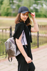 Beautiful stylish brunette girl in a white T-shirt and black pants with a backpack on his shoulder. Vertical photo