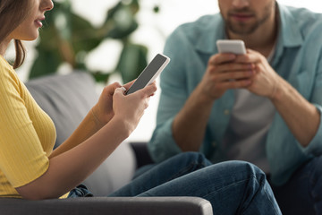 Cropped view of addicted couple using smartphones on couch