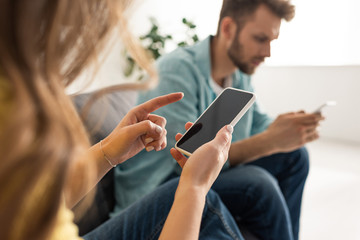 Selective focus of woman holding smartphone with blank screen near boyfriend on sofa
