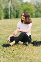 Fototapeta premium Stylish hipster girl in a white T-shirt sitting on a grass lawn outdoors posing
