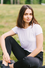Naklejka na ściany i meble Stylish hipster girl in a white T-shirt sitting on a grass lawn outdoors posing