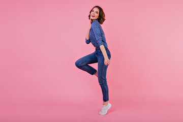 Full-length portrait of sporty girl with wavy hair. Indoor shot of jumping young woman in jeans and blue shirt.