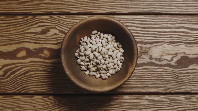 Dried white beans fill a wooden dish. Top view, stop motion.