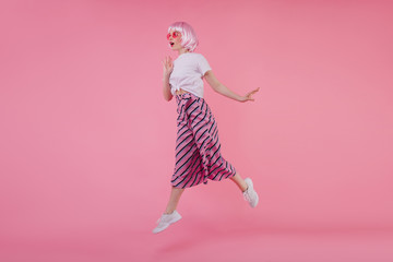 Blissful european young woman in elegant white sneakers jumping during phtooshoot. Studio portrait of joyful lady wearing peruke dancing on pink background.