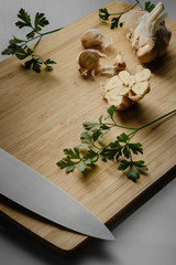 Garlic bulb cut in half. Bamboo cutting board, knife and parsley. Vertical orientation.
