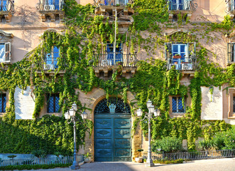 Fototapeta na wymiar facade detail of city hall building in the historic center of Agrigento overgrown with ivy, door and windows and decoration. Agrigento Sicily. Italy