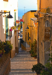 Fototapeta na wymiar Narrow street with view on the roofs and balcony of old center of Agrigento with mediterranean sea in background. Sicily Italy