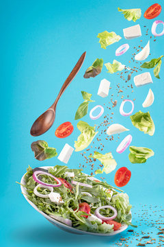 Flying salad isolated on blue background. Greek salad: red tomatoes, cheese, lettuce, onion and seeds.