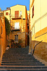Fototapeta na wymiar View of a narrow street with steps, old buildings and facades in the historical city of Agrigento in Sicily, Italy