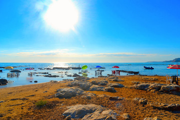 Tables and chairs immersed in the sea water under colorful green, blue and red umbrellas with the background of sea horizon and boats, Agrigento Italy