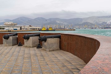 Novorossiysk, Russia - March 25, 2020. - Installation of coastal battery at the observation deck. Three old cannons are directed to sea. Blurred background of terminals of sea trading port.