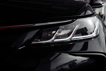 Obraz na płótnie Canvas headlight of modern prestigious black car close up. Close up photo of modern car, detail of headlight. Headlight car Projector LED of a modern luxury technology and auto detail. selective focus