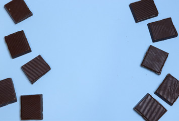 a bar of dark chocolate is broken into pieces, laid out on a blue background. Place for text,...