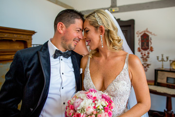 Happy beautiful wedding couple posing in room. blonde bride holding a bouquet of flowers in hands