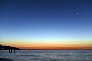 The last light of day creates dramatic colors in the sky over the sea. New moon rising.