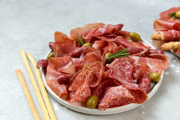 Prosciutto jamon Parma ham salami smoked sausage and olives with grissini breadsticks on a white plate. Serving appetizers for an aperitif, lunch, dinner and holiday. catering, food delivery