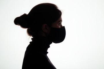 silhouette of confident young woman in protective mask on studio background, girl looking straight readynto deal with danger, concept health and safety