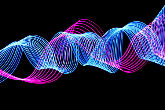 Long exposure photograph of neon purple and blue colour in an abstract swirl, parallel lines pattern against a black background. Light painting photography.