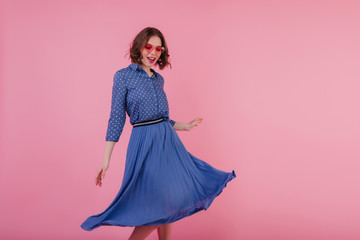 Refined white girl with wavy hair dancing on pink background. Studio photo of winsome european lady wears blue midi skirt and blouse.