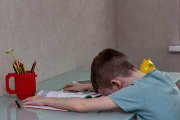Obraz premium Tired sad boy studying at home online during quarantine. ired sad boy studying at home online. Fall asleep at the desk while doing homework.