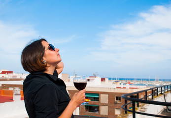Woman enjoy blue sky from her balcony with glass of red wine. Stay home. Lonely woman.