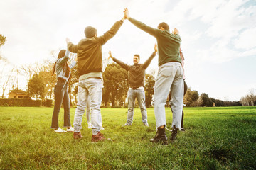 Group of six friends at the park at sunset holding hands in the air - Teamwork - Concept of unity and collaboration