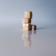A small stack of brown sugar cubes sitting in the centre of the frame.  The image is reflected back on the shiny surface and sits against a plain background with space all around the frame.