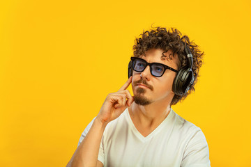 Portrait of happy bearded man with curly hair pointing finger at screen isolated over yellow background. Guy in blue sunglasses and headphones pick on great idea.