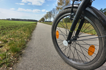 Front wheel of a bicycle on a paved bicycle path, which disappears next to a row of trees in the...