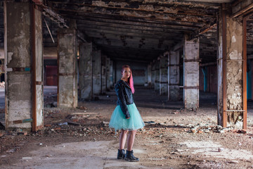 Fototapeta na wymiar Portrait of a young girl with pink hair standing inside of collapsed building surrounded by ruins