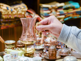 Female hand holds a souvenir Turkish tea glass with a spoon.